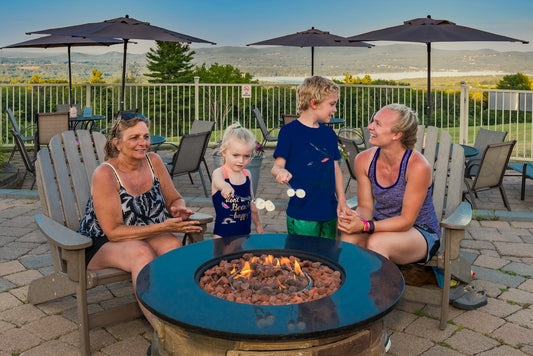 A family toasting marshmallows over a gas fire pit on the Steele Hill hilltop patio at dusk