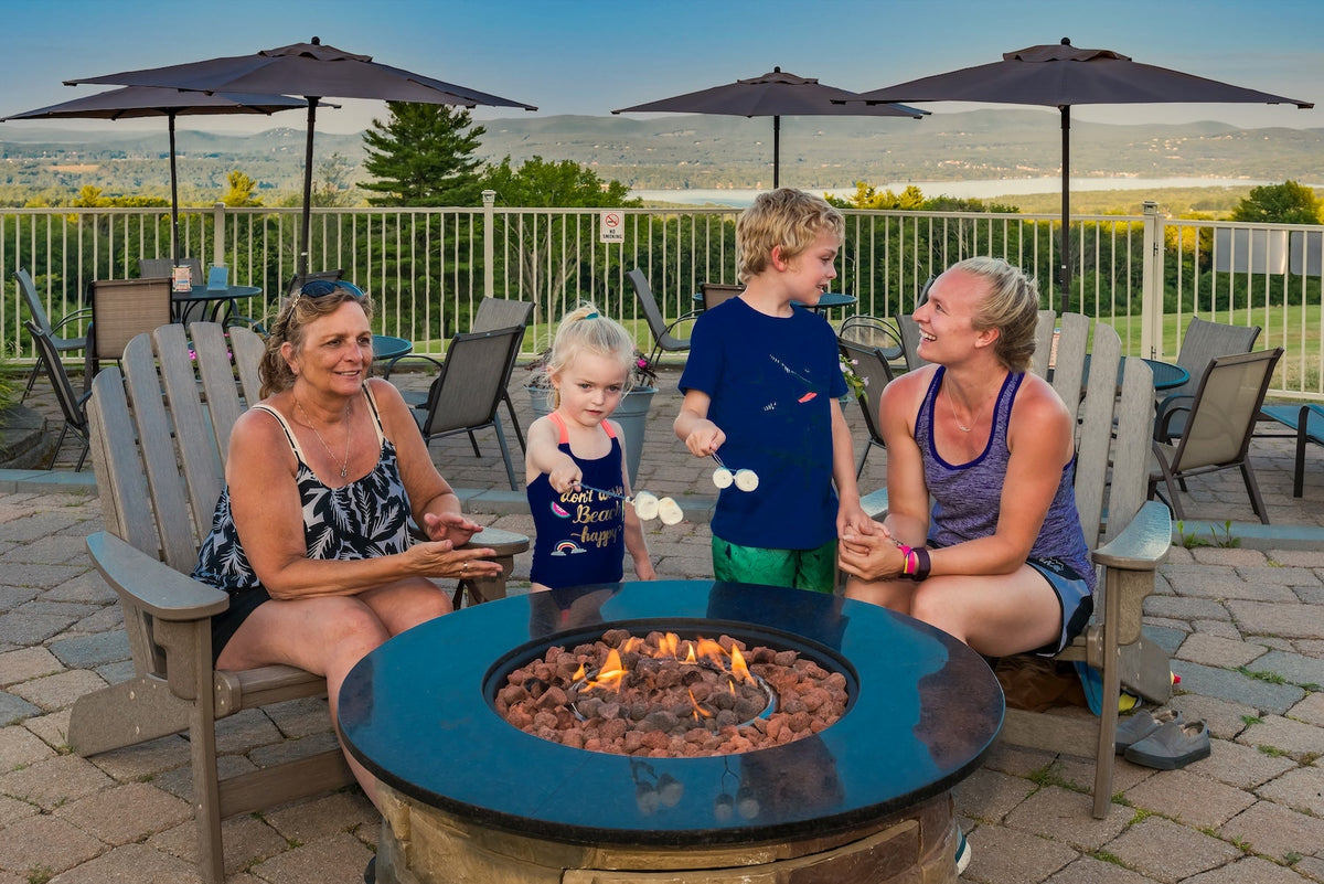 A family toasting marshmallows over a gas fire pit on the Steele Hill hilltop patio at dusk