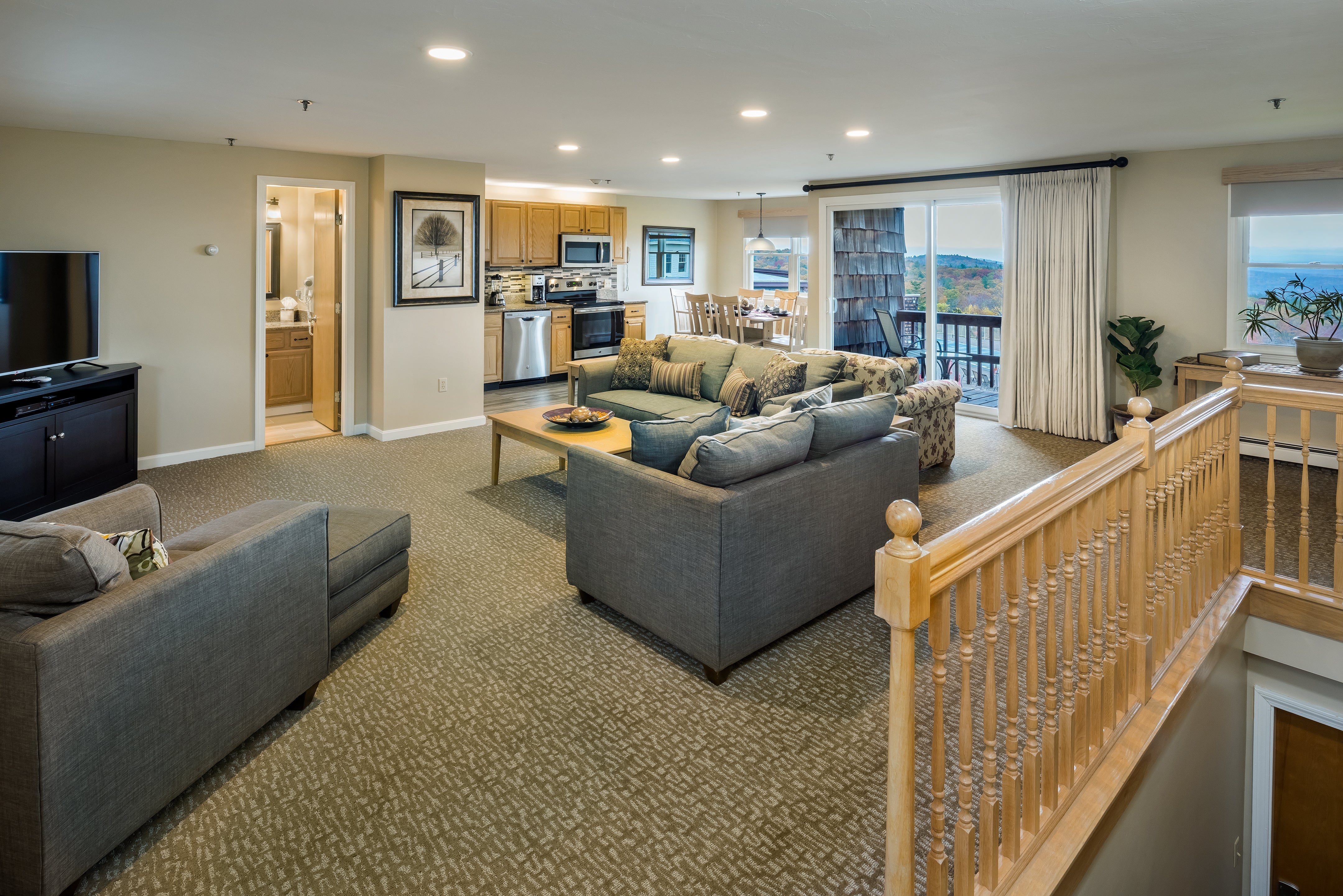Open-plan Steele Hill suite with two sofas, a full kitchen and dining area beside balcony doors to the lake