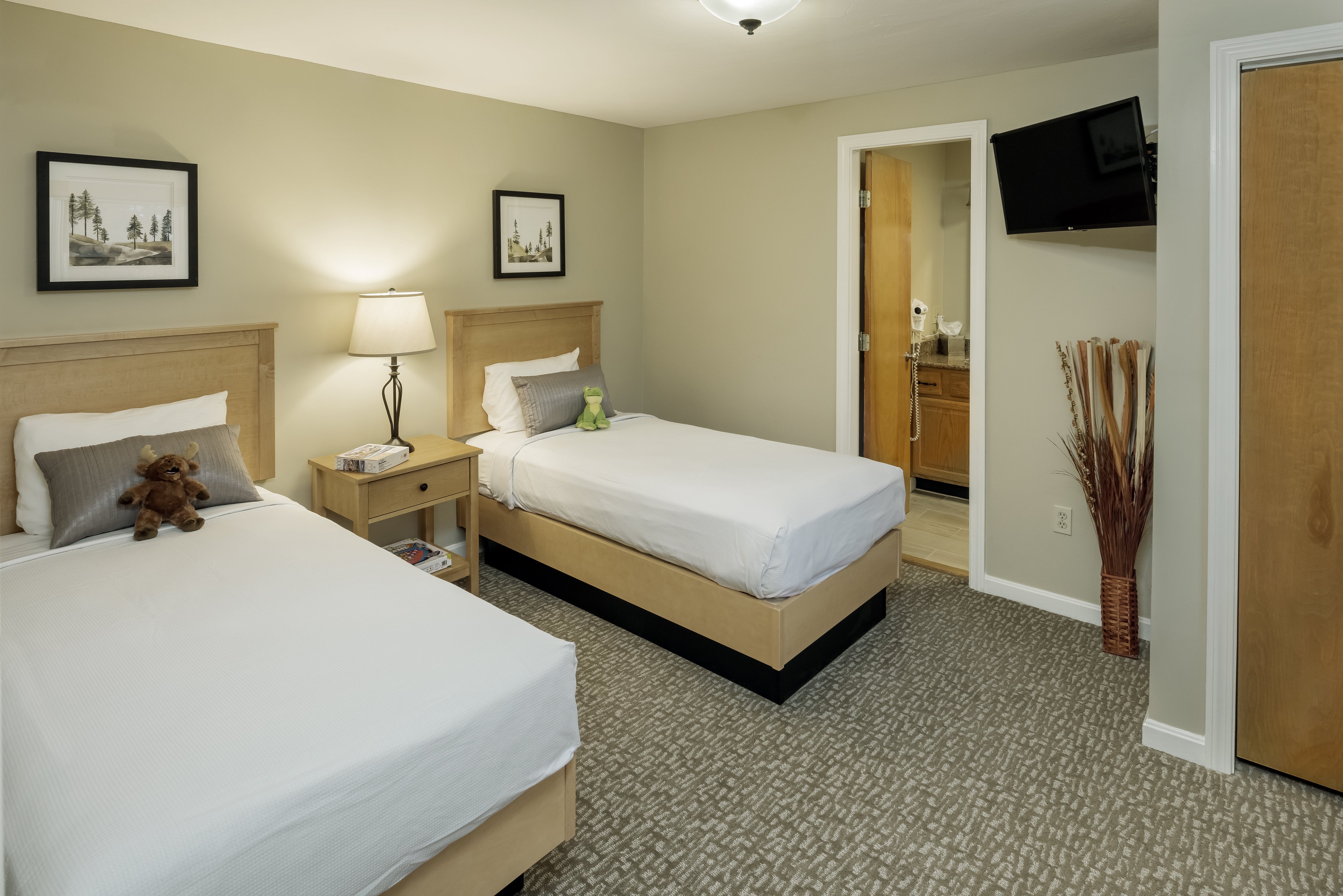 Bedroom with two twin beds, a teddy bear, framed forest prints and an open bathroom door