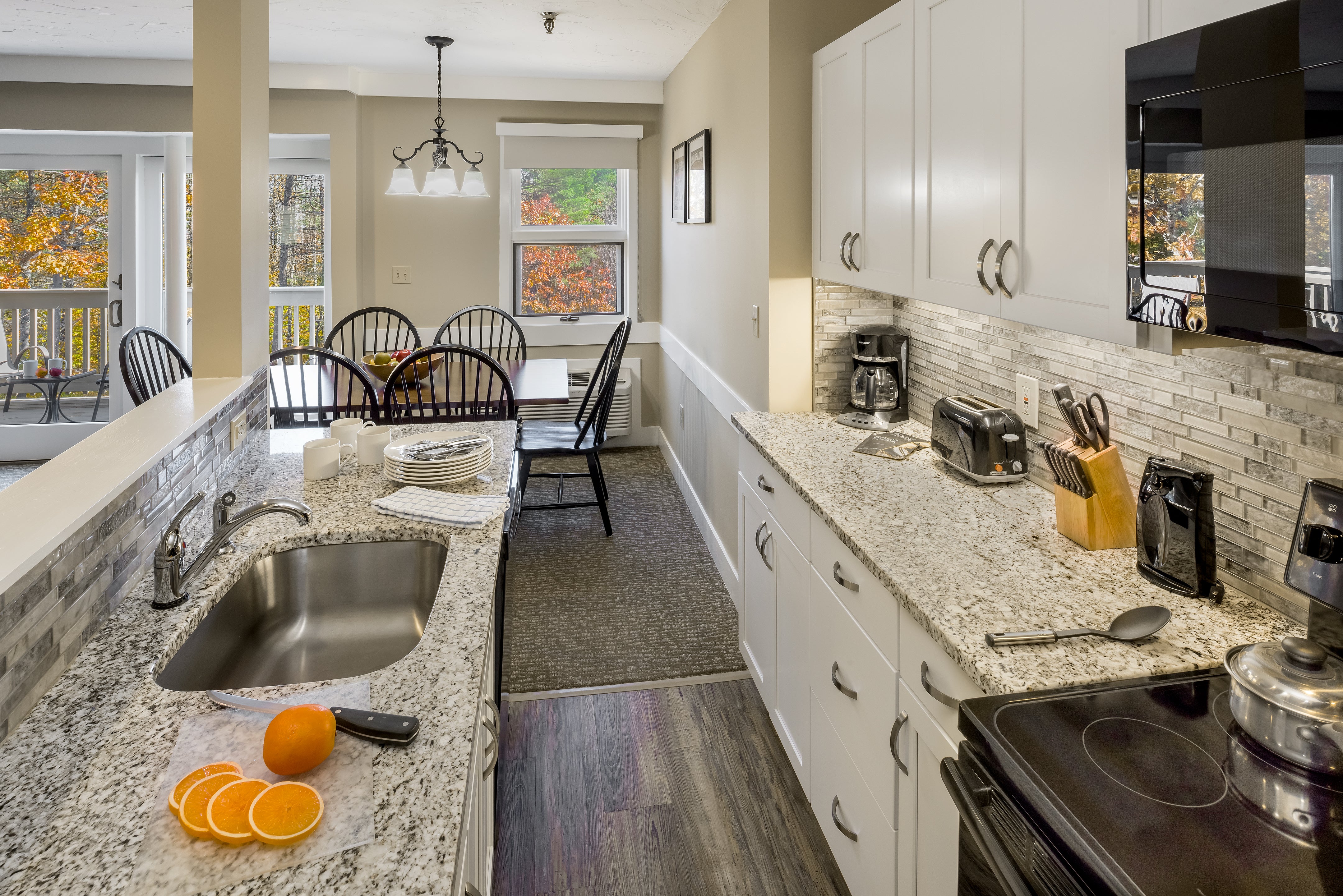 Galley kitchen with granite counters, sliced oranges and a dining table by fall-colored windows
