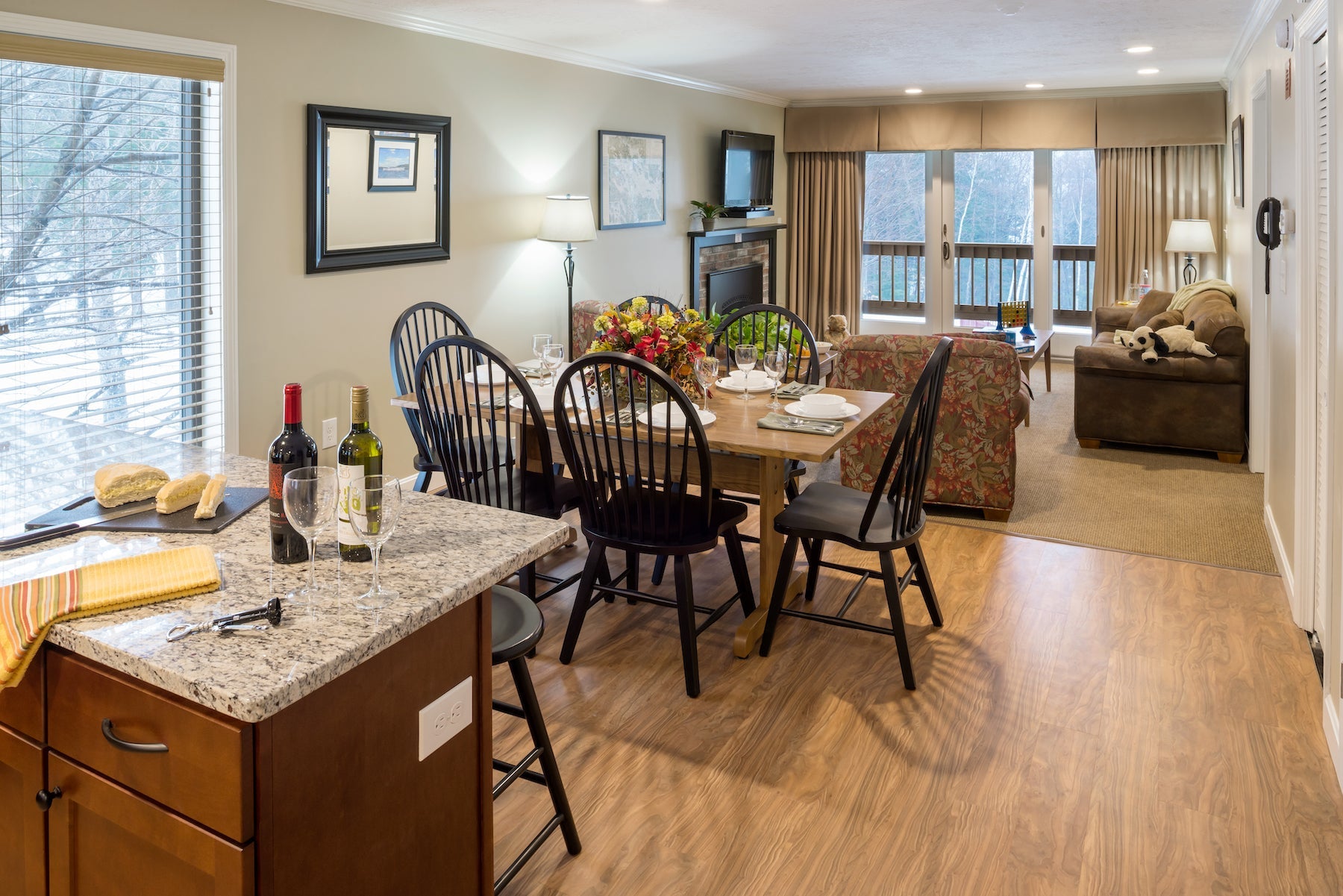 Condo kitchen island with wine glasses opening onto a dining table and living room with fireplace