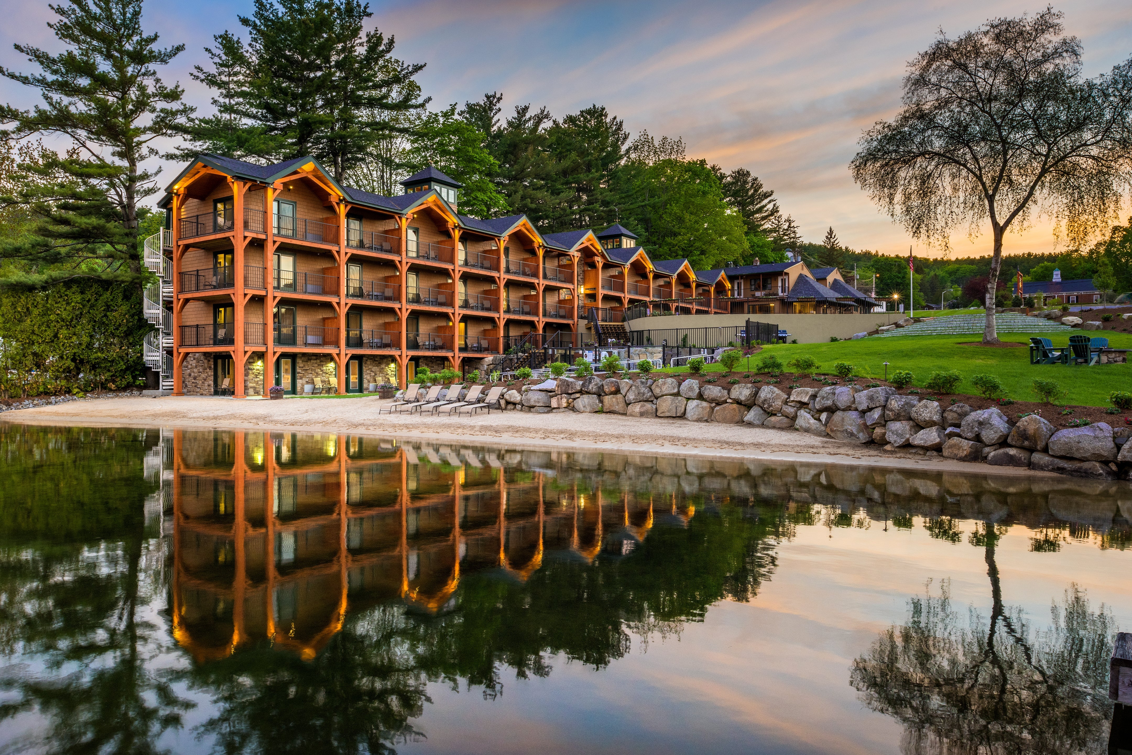 Timber-frame lakeside lodge at Center Harbor Inn glowing at dusk, mirrored in calm Lake Winnipesaukee