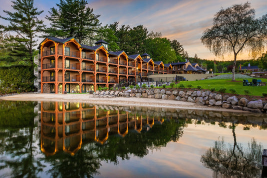 The Center Harbor Inn's timber-frame lakeside lodge glowing at dusk, mirrored in calm Lake Winnipesaukee