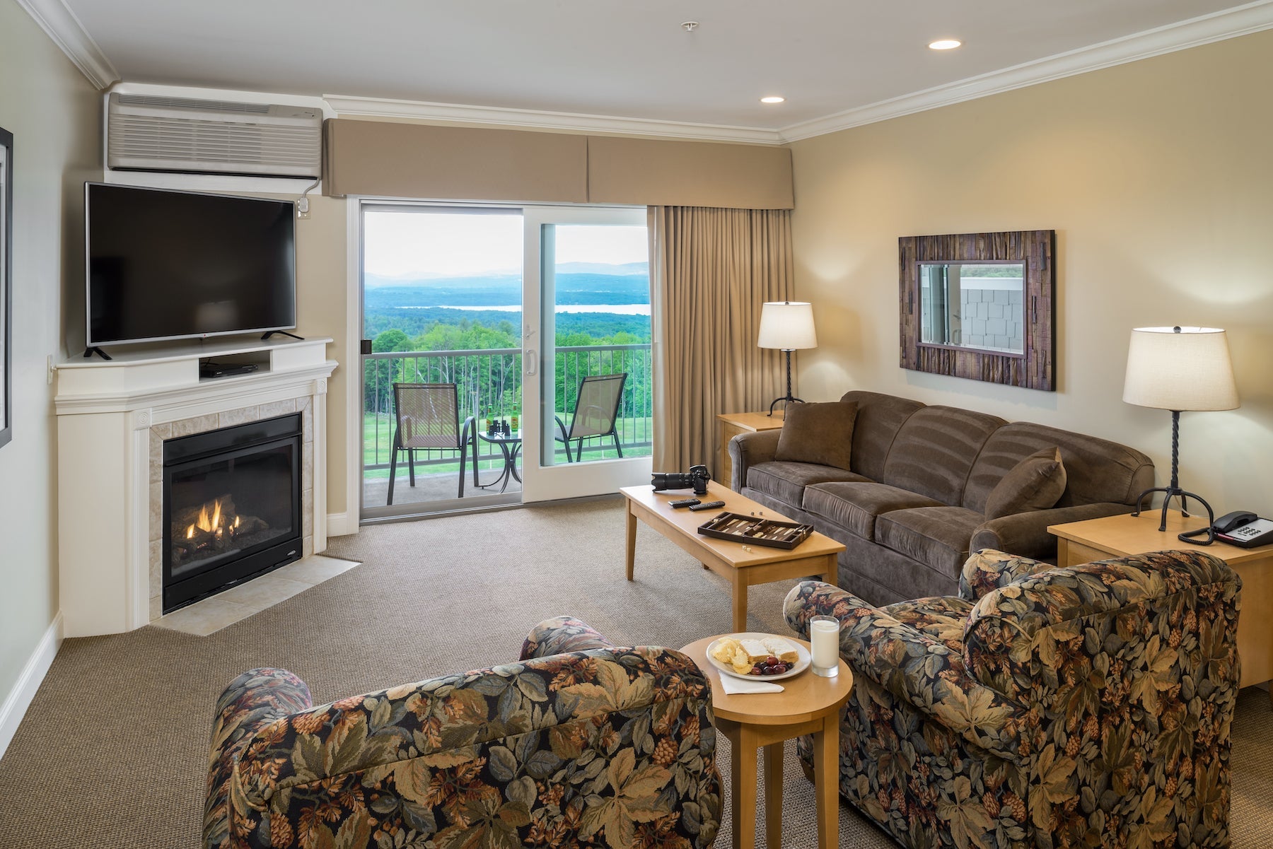 Suite living room with a lit gas fireplace, TV and balcony doors framing a distant lake view