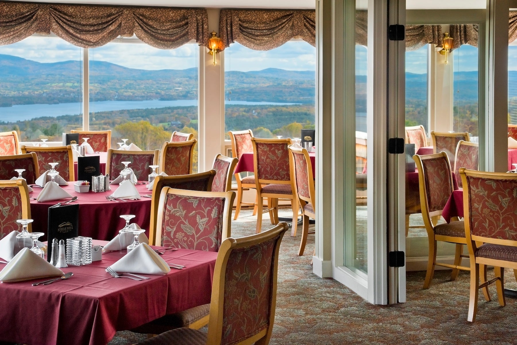 Steele Hill dining room set with burgundy linens beside floor-to-ceiling windows over the lake