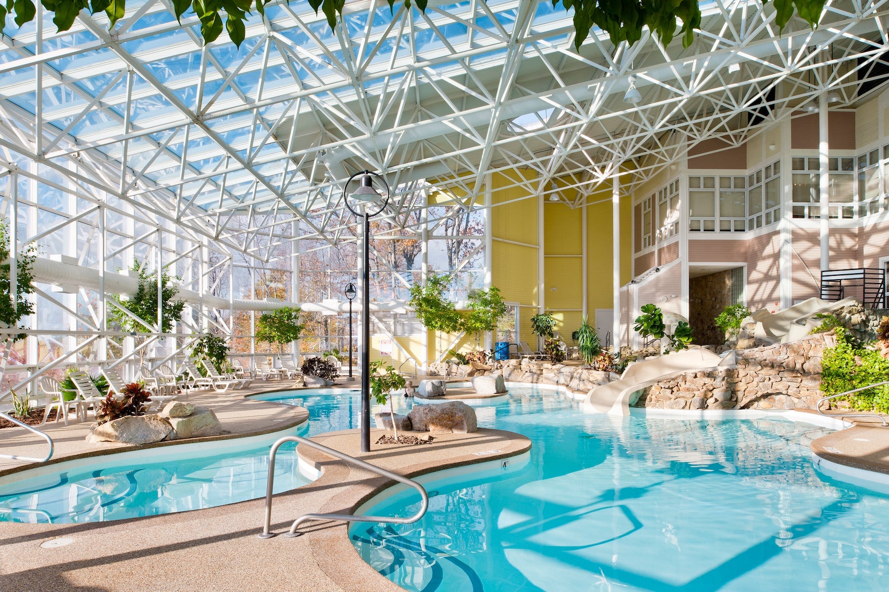Sunlit indoor pool at Steele Hill with turquoise water, a slide and a glass truss roof