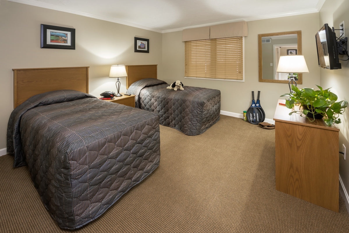 Second bedroom with two twin beds, wood headboards, a dresser and a wall-mounted TV