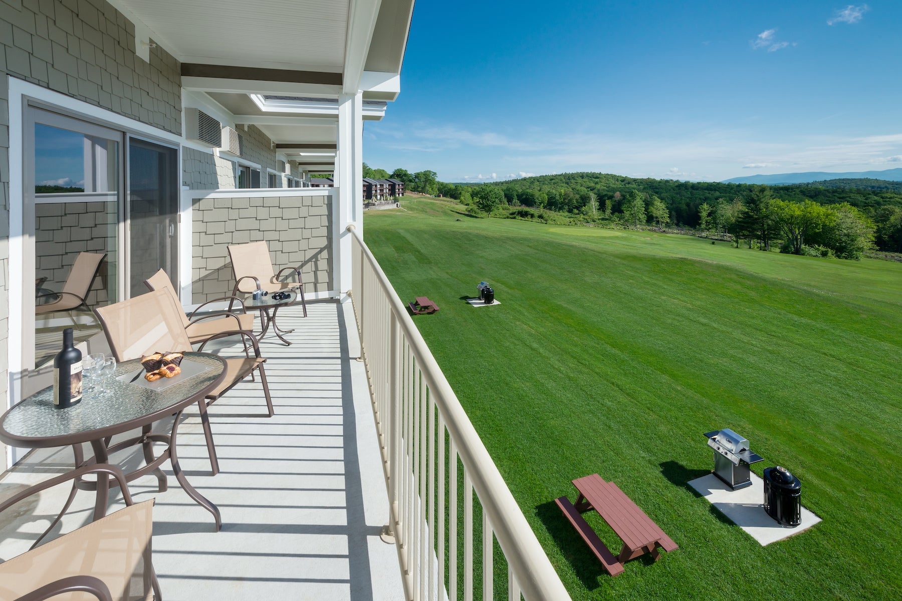 Steele Hill balcony with patio tables and chairs above a wide green lawn with grills