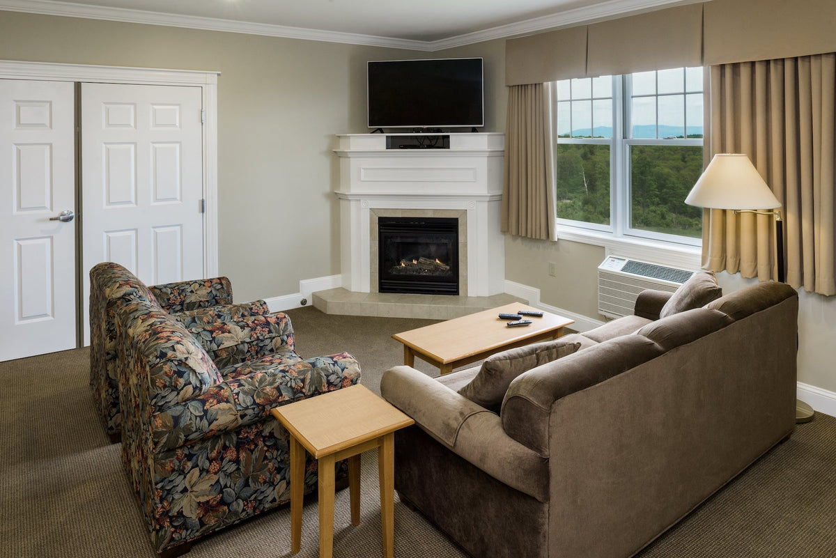 Center Harbor Inn sitting area with a corner gas fireplace, sofa and windows over wooded hills