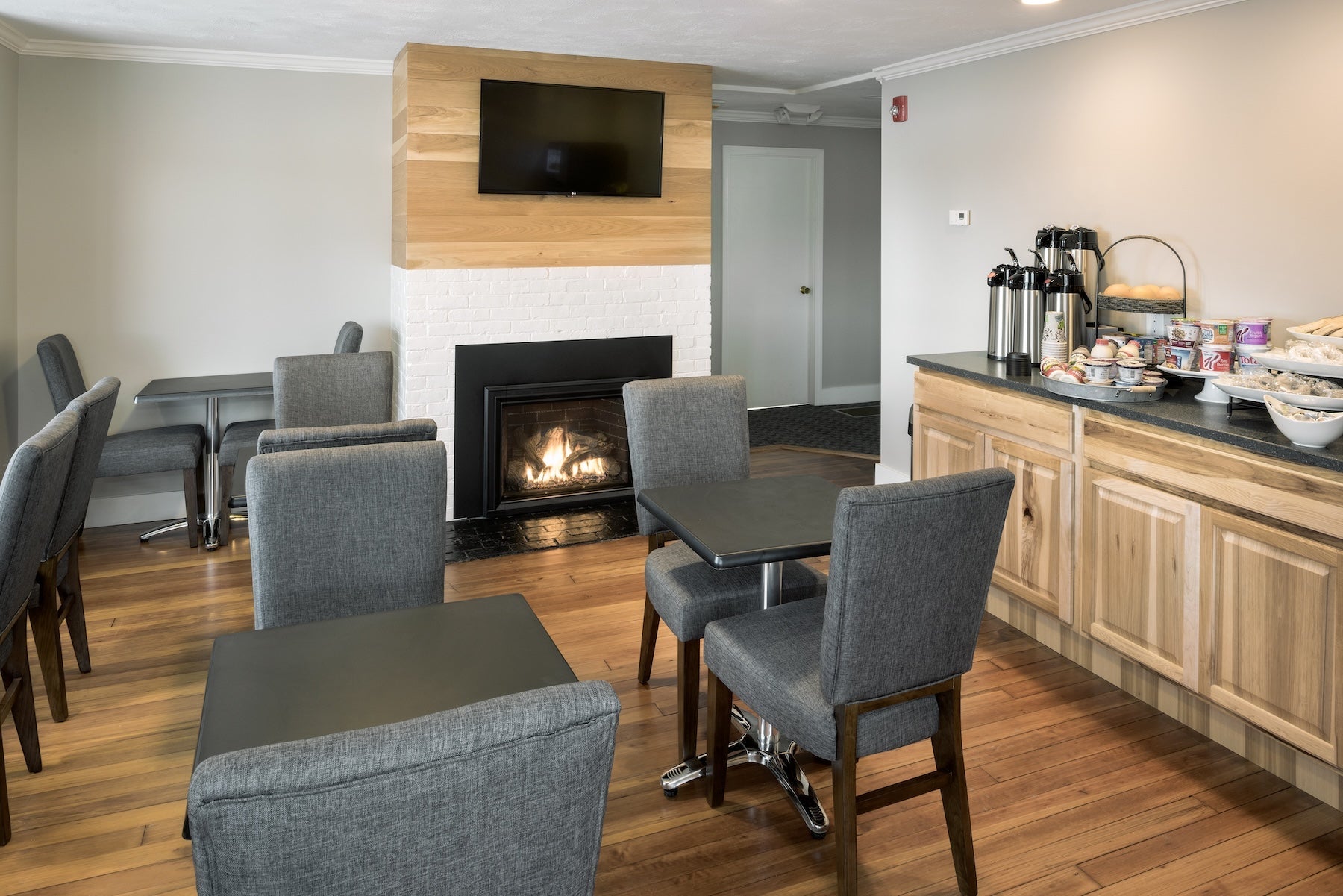 Center Harbor Inn breakfast room with cafe tables, a lit fireplace and a coffee and pastry counter
