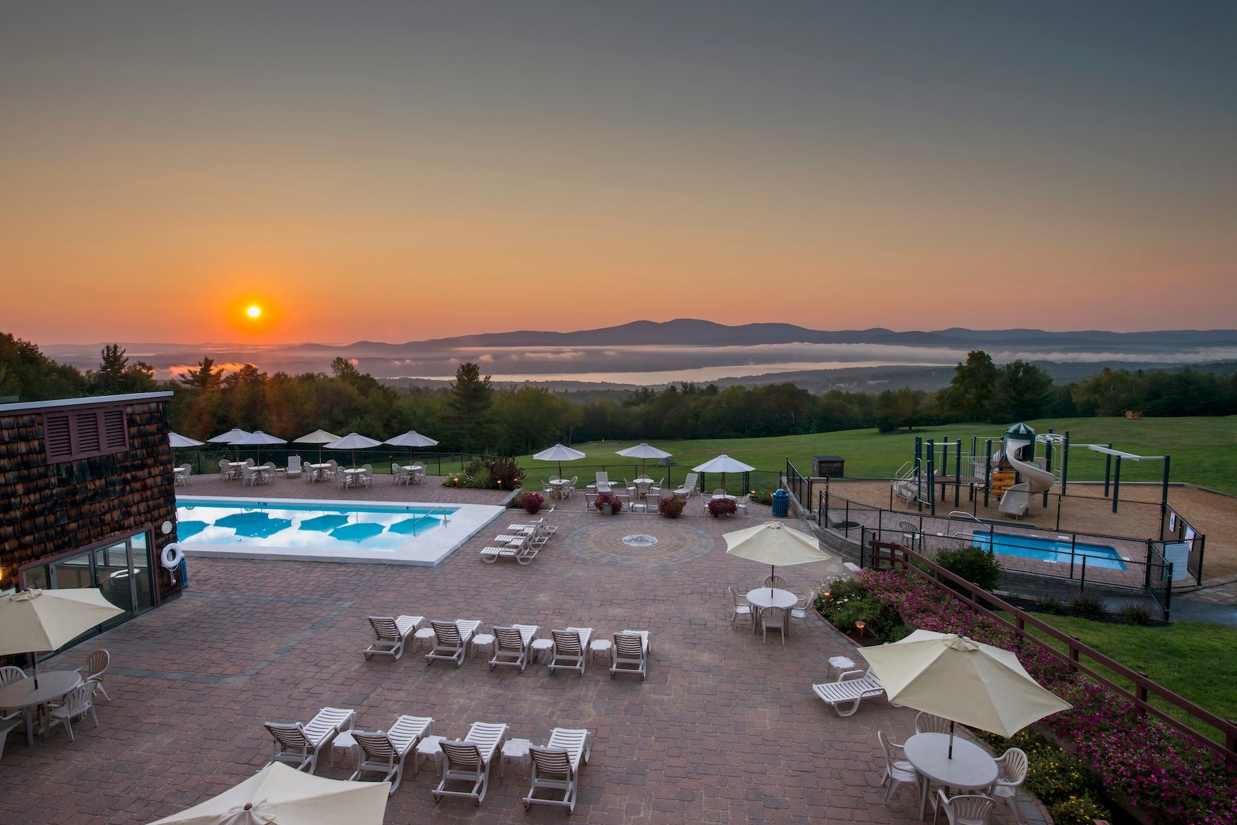 Sunrise over misty hills behind a hilltop pool patio with white loungers and umbrellas