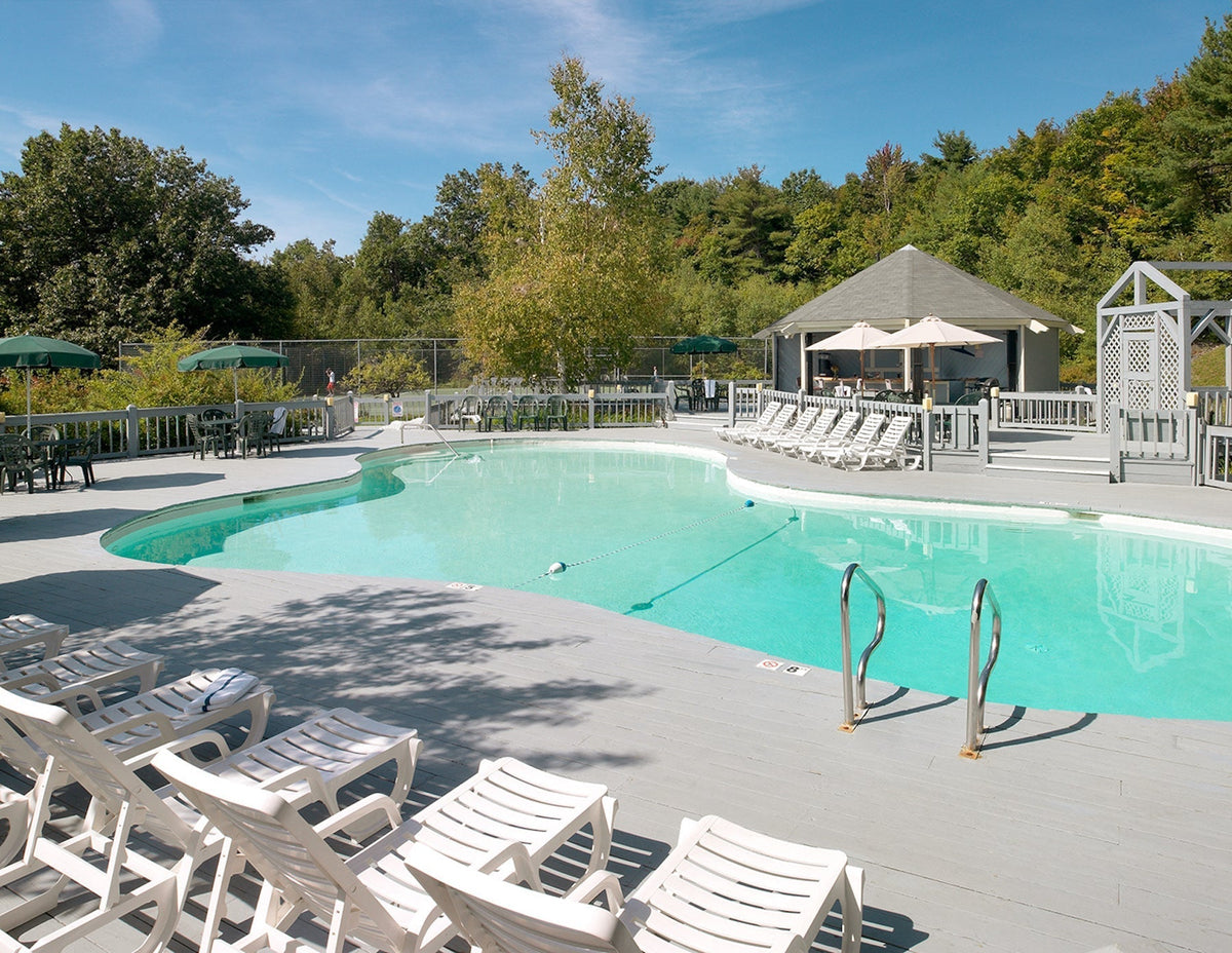 Kidney-shaped outdoor pool at Steele Hill with lounge chairs and a gazebo backed by pine woods