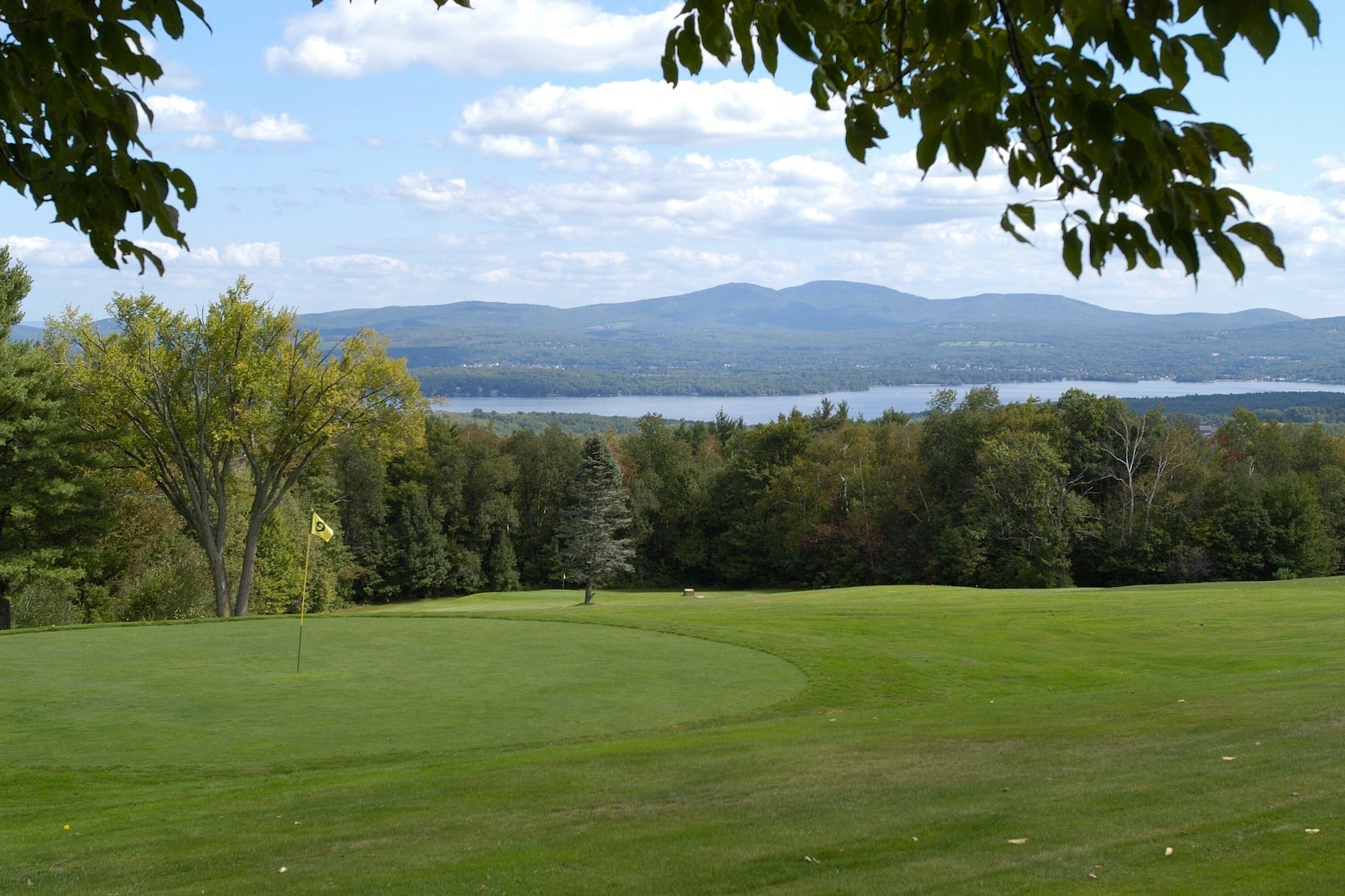 Golf green with a yellow flag at Steele Hill overlooking wooded hills and a long lake