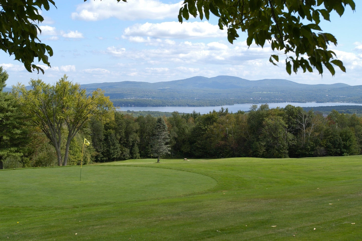 Golf green with a yellow flag at Steele Hill overlooking wooded hills and a long lake