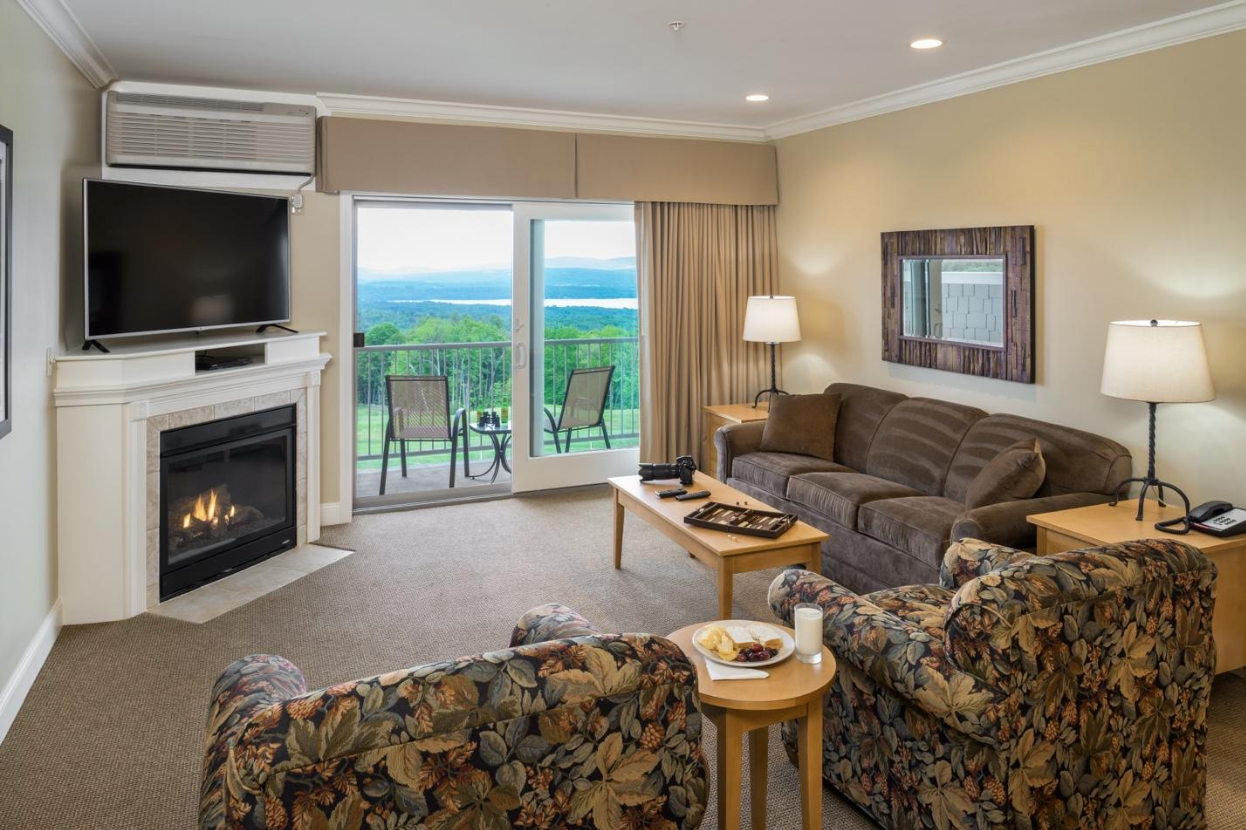 Suite living room with gas fireplace, TV, and sliding doors to a balcony above the lake and mountains